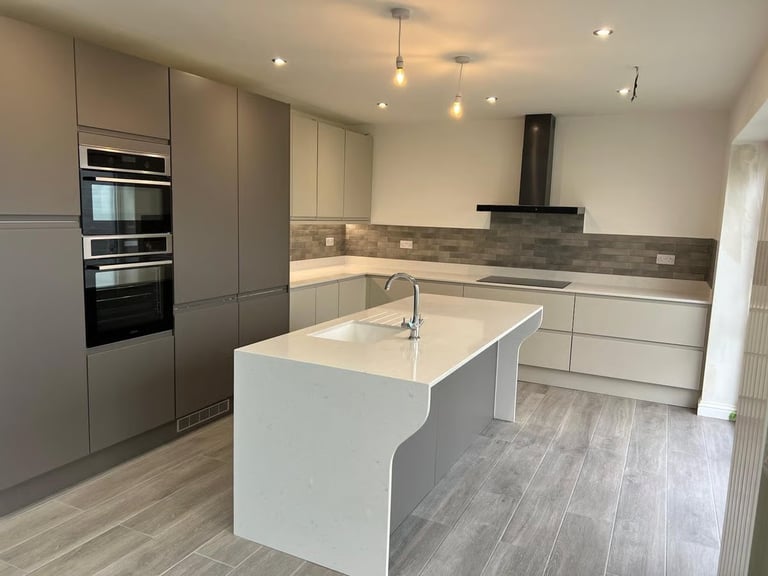 Modern kitchen with white central island, gray cabinetry, stainless steel appliances, and gray tile backsplash