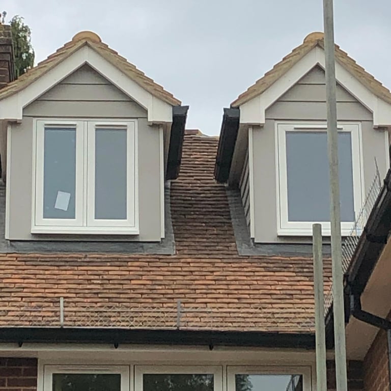 Residential house with twin dormer windows, red clay tile roof, and white-trimmed casement windows on brick facade